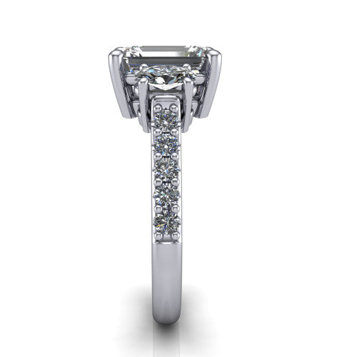 Poppy emerald three stone engagement ring in Platinum, side profile showing the round side stone and the pavé diamonds running down the shank