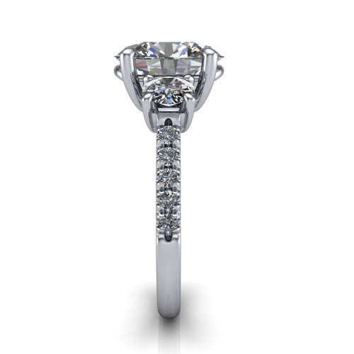 Celeste oval three stone engagement ring in Platinum, side profile showing the round side stone and the pavé diamonds running down the shank