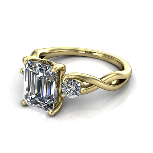 Lydia emerald three stone engagement ring in 18K Yellow Gold, three-quarter perspective showing the step-cut emerald center diamond flanked by two round side diamonds on a woven infinity shank