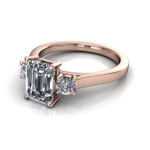 Olivia emerald three stone engagement ring in 18K Rose Gold, three-quarter perspective showing the step-cut emerald center diamond flanked by two round side diamonds on a squared flat-top shank