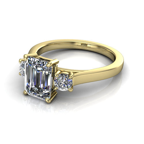 Olivia emerald three stone engagement ring in 18K Yellow Gold, three-quarter perspective showing the step-cut emerald center diamond flanked by two round side diamonds on a squared flat-top shank