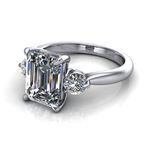 Juniper emerald three stone engagement ring in Platinum, three-quarter perspective showing the step-cut emerald center diamond flanked by two round side diamonds on a rounded plain band