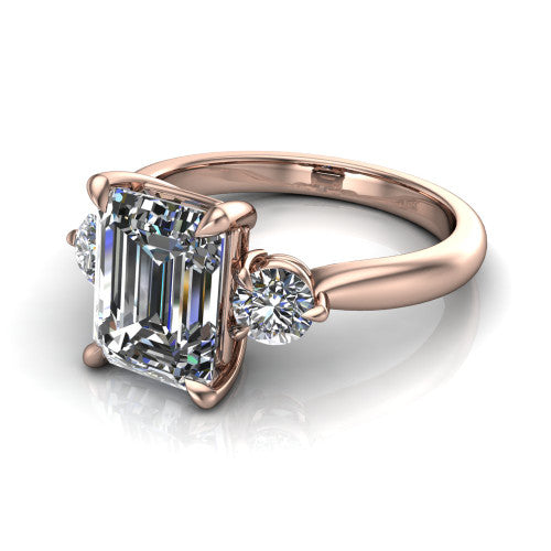 Juniper emerald three stone engagement ring in 18K Rose Gold, three-quarter perspective showing the step-cut emerald center diamond flanked by two round side diamonds on a rounded plain band