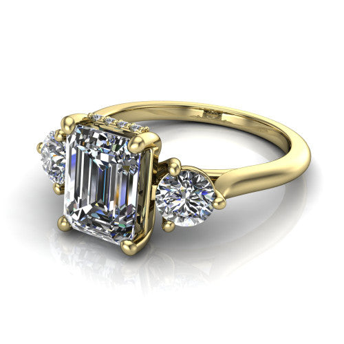 Edith emerald hidden halo engagement ring in 18K Yellow Gold, three-quarter perspective showing the step-cut emerald center diamond flanked by two round side diamonds with a hidden pave halo beneath the center stone