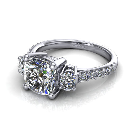 Poppy cushion three stone engagement ring in Platinum, three-quarter perspective showing the center diamond between two round side stones above a pav&eacute; shank