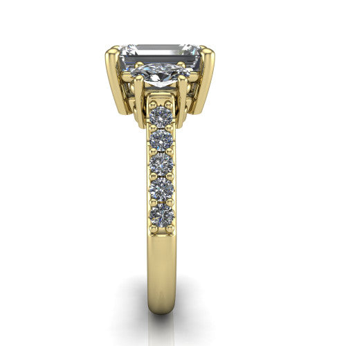 Poppy emerald three stone engagement ring in 18K Yellow Gold, side profile showing the round side stone and the pav&eacute; diamonds running down the shank