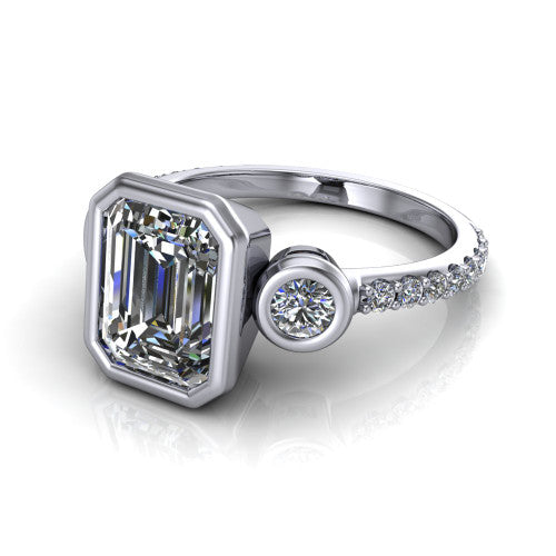 Chloe emerald three stone engagement ring in Platinum, three-quarter perspective showing the bezel-set center between two bezel-set round side stones above a pav&eacute; shank