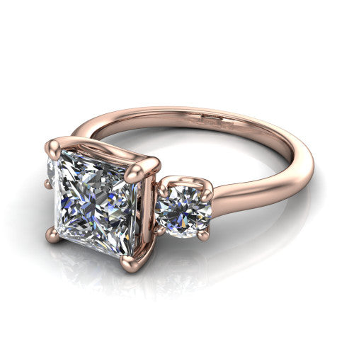 Emma princess three stone engagement ring in 18K Rose Gold, three-quarter perspective showing the center diamond between two round side stones on a slim polished band