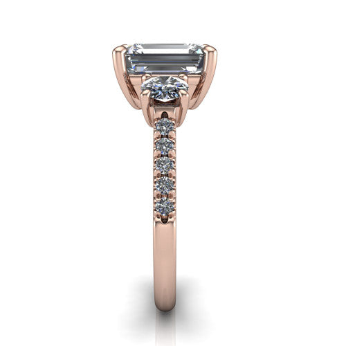 Celeste emerald three stone engagement ring in 14K Rose Gold, side profile showing the round side stone and the pav&eacute; diamonds running down the shank