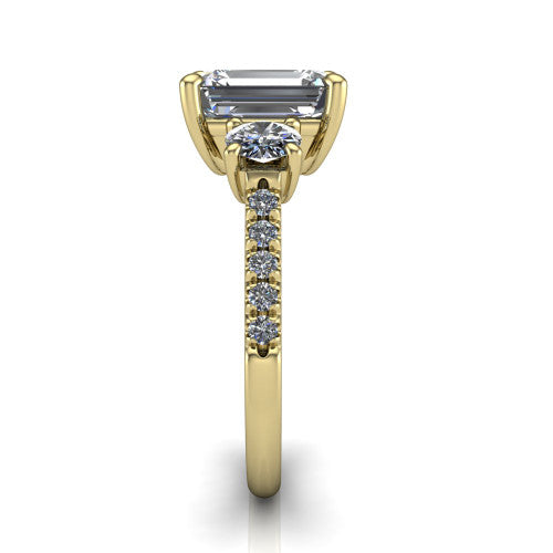 Celeste emerald three stone engagement ring in 14K Yellow Gold, side profile showing the round side stone and the pav&eacute; diamonds running down the shank