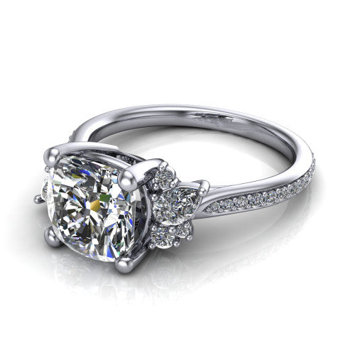 Mila cushion three stone engagement ring in Platinum, three-quarter perspective showing the center diamond flanked by round accent clusters above a pav&eacute; shank