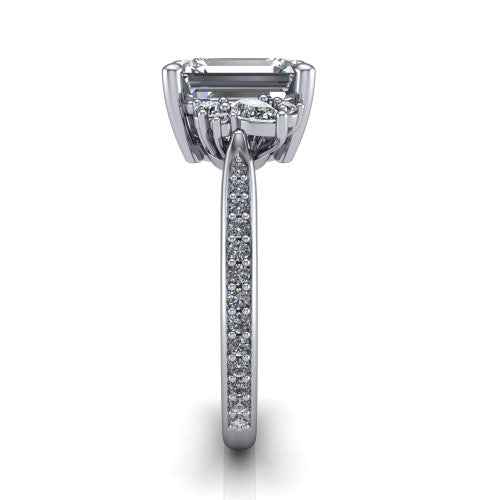 Mila emerald three stone engagement ring in Platinum, side profile showing the round accent cluster and the pav&eacute; diamonds running down the shank