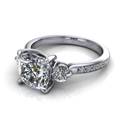 Blake cushion three stone engagement ring in Platinum, three-quarter perspective showing the center diamond between two round side stones above a pav&eacute; shank