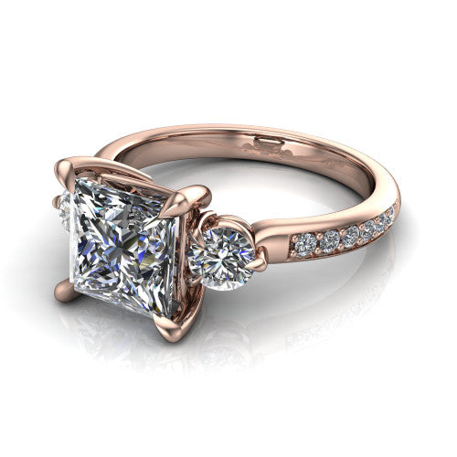 Blake princess three stone engagement ring in 18K Rose Gold, three-quarter perspective showing the center diamond between two round side stones above a pav&eacute; shank