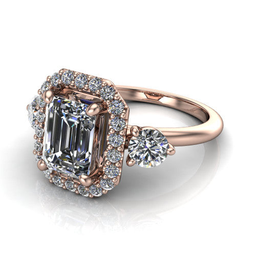 Carol emerald three stone halo engagement ring in 18K Rose Gold, three-quarter perspective showing the emerald center in a squared pav&eacute; halo flanked by two round side stones above a plain band