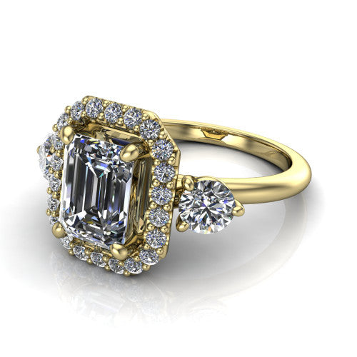 Carol emerald three stone halo engagement ring in 18K Yellow Gold, three-quarter perspective showing the emerald center in a squared pav&eacute; halo flanked by two round side stones above a plain band
