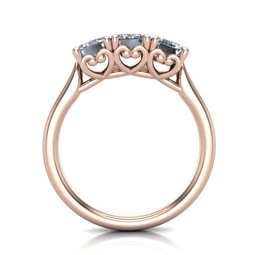 Amora emerald three stone engagement ring in 18K Rose Gold, through-finger side profile showing the heart filigree scroll gallery beneath the three stones