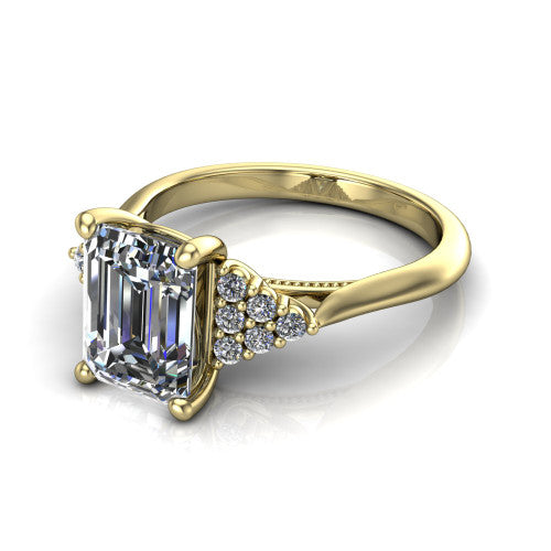 Raya emerald three stone engagement ring in 18K Yellow Gold, three-quarter perspective showing the center stone flanked by a trio diamond cluster on each shoulder above a slim milgrain band