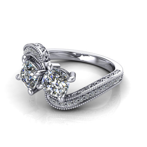 Stevie cushion three stone engagement ring in Platinum, three-quarter perspective showing two brilliant cushion-cut diamonds set diagonally on filigree shoulders with milgrain edges and a pave center band