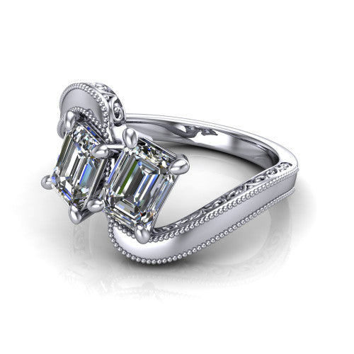 Logan emerald three stone engagement ring in Platinum, three-quarter perspective showing two step-cut emerald diamonds set diagonally on engraved filigree shoulders with milgrain edges