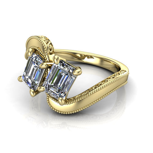 Logan emerald three stone engagement ring in 18K Yellow Gold, three-quarter perspective showing two step-cut emerald diamonds set diagonally on engraved filigree shoulders with milgrain edges