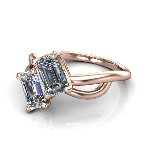 Mya emerald three stone engagement ring in 18K Rose Gold, three-quarter perspective showing two step-cut emerald diamonds set diagonally on a polished infinity-loop shank