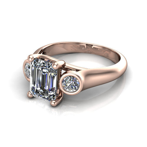 Rory emerald three stone engagement ring in 18K Rose Gold, three-quarter perspective showing the emerald center diamond between two bezel-set round side stones